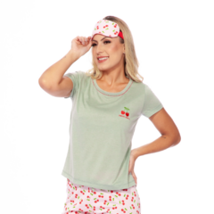 O pijama é composto por uma camiseta de cor verde clara e calças estampadas. A camiseta tem um ajuste relaxado e apresenta um pequeno design bordado de cereja no peito esquerdo. As calças são brancas com uma estampa colorida