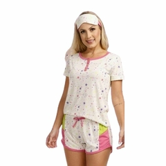 O pijama curto feminino na imagem tem uma blusa branca com estampas de estrelas coloridas e um short rosa. A blusa tem um detalhe de acabamento em rosa ao longo do decote e um laço rosa na frente. O short do pijama é predominantemente rosa, com uma faixa 