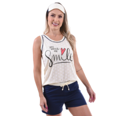 O pijama baby doll na imagem é composto por um top e shorts. O top é branco com pequenos pontos (poá), tem uma bainha preta e apresenta a frase “YOU MAKE ME SMILE” com um coração vermelho entre “ME” e “SMILE”. Os shorts são de cor azul sólida com um cordã