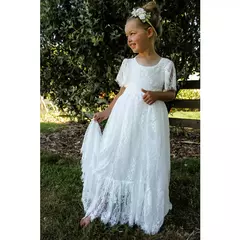 Menina sorridente vestindo um longo vestido branco de renda, ideal para daminha de casamento, batizado ou primeira comunhão, em um ambiente natural.