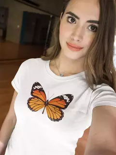 Camisa branca BabyLook com estampa de borboleta laranja e preta, usada por uma mulher sorridente.