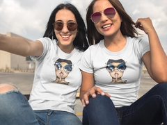 Duas mulheres sorrindo usando camisetas brancas com estampa de rostos.