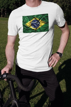 Homem usando uma camisa branca com estampa da bandeira do Brasil, em um ambiente ao ar livre.