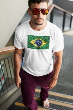 Homem usando uma camisa branca com estampa da bandeira do Brasil, óculos de sol e calça roxa, descendo uma escada.