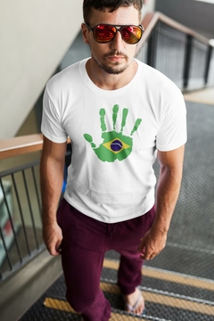 Homem usando uma camisa branca com um design de mão verde e azul, simbolizando o Brasil, enquanto desce uma escada.