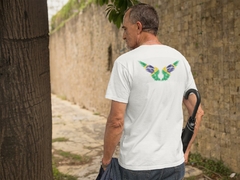 Homem usando uma camisa branca com estampa de asas nas costas, inspirada nas cores da bandeira do Brasil, caminhando em um caminho ao ar livre.