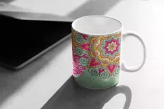 Caneca branca com estampa de mandala colorida em tons de rosa, laranja e verde, sobre superfície clara.