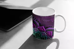 Caneca branca com estampa de mandala colorida em tons de roxo e verde, apoiada em uma superfície cinza.