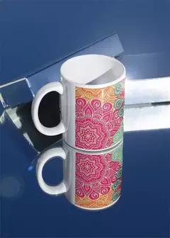 Caneca branca com design de mandala colorida em tons de rosa e verde, refletida em superfície espelhada.