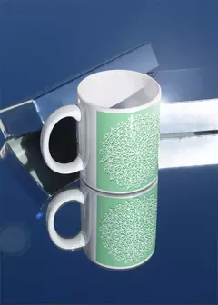 Caneca branca com design de mandala verde, refletida em superfície espelhada.