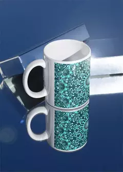 Caneca branca com estampa de mandala em tons de azul e verde, refletida em uma superfície espelhada.