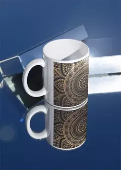 Caneca branca com estampa de mandala em tons dourados, refletindo em superfície azul.