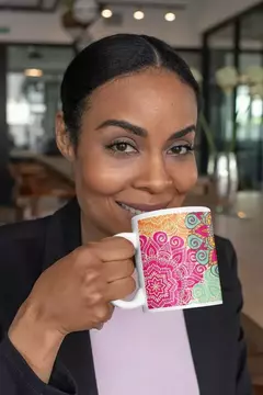 Mulher sorrindo enquanto segura uma caneca branca com design de mandala colorida.