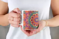 Caneca branca com estampa de mandala colorida, sendo segurada por uma pessoa.