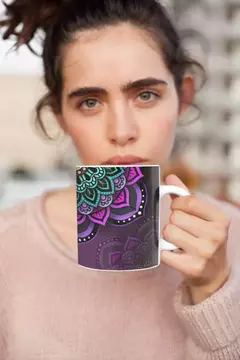 Caneca branca com estampa de mandala colorida em tons de verde e rosa, sendo segurada por uma mulher com olhar sério.