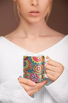 Caneca branca com design de mandala colorida, segurada por uma mulher com suéter branco.