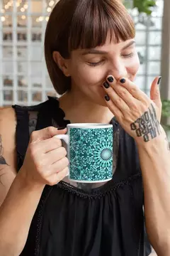 Mulher segurando uma caneca branca com estampa de mandala em tons de verde, sorrindo e cobrindo a boca com a mão.