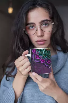 Mulher segurando uma caneca branca com estampa de mandala colorida, vestindo um suéter cinza.