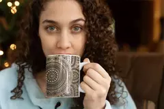 Uma mulher segurando uma caneca branca com estampas de mandala, olhando diretamente para a câmera.