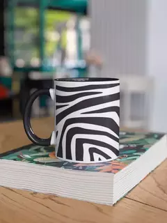 Caneca de porcelana com estampa de zebra, em cima de uma mesa de madeira, ao lado de um livro ilustrado.