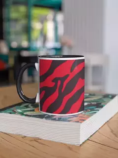 Caneca de porcelana com estampa animal print em vermelho e preto, apoiada sobre um livro, em um ambiente moderno.