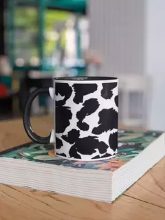 Caneca de porcelana com estampa animal print em preto e branco, repousando sobre uma mesa de madeira ao lado de um livro.