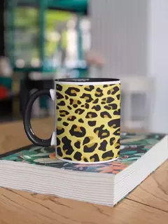 Caneca de porcelana com estampa animal print em amarelo e preto, apoiada sobre um livro em uma mesa de madeira.