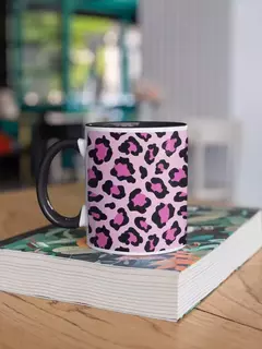 Caneca de porcelana com estampa animal print em tons de rosa e preto, sobre um livro em uma mesa de madeira.