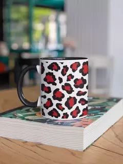 Caneca de porcelana com estampa de onça em preto e vermelho, apoiada sobre um livro em uma mesa de madeira.