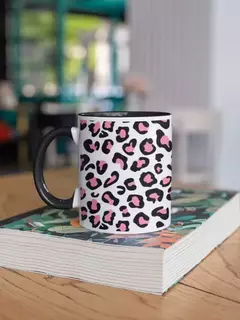 Caneca de porcelana com estampa animal print em preto e rosa, apoiada sobre um livro em uma mesa de madeira.