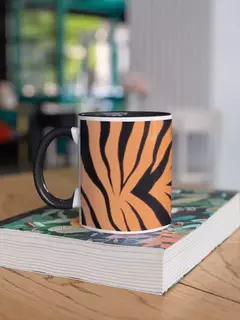 Caneca de porcelana com estampa de animal print nas cores laranja e preto, apoiada sobre uma mesa com um livro.