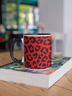 Caneca de porcelana com estampa animal print em fundo vermelho, descansando sobre um livro em uma mesa de madeira.