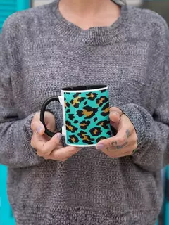 Caneca de porcelana com estampa animal print em fundo azul, sendo segurada por uma pessoa com suéter cinza.