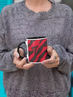 Caneca de porcelana com estampa animal print em vermelho e preto, sendo segurada por uma pessoa com suéter cinza.