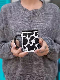 Caneca de porcelana com estampa animal print em preto e branco, sendo segurada por uma pessoa em um suéter cinza.