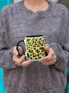 Caneca de porcelana com estampa animal print em amarelo e preto, segurada por uma pessoa vestindo um suéter cinza.