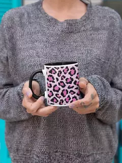 Caneca de porcelana com estampa de animal print em rosa e preto, segurada por uma pessoa vestindo um suéter cinza.