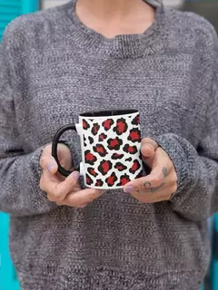 Caneca de porcelana com estampa animal print nas cores branca, preta e vermelha, segurada por uma mulher vestindo um suéter cinza.