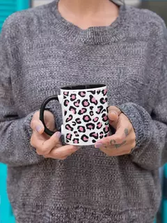 Caneca de porcelana com estampa de animal print, segurada por uma pessoa vestindo um suéter cinza.