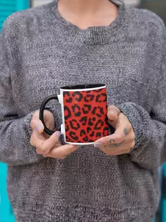 Caneca de porcelana com estampa de animal print em vermelho e preto, segurada por uma pessoa usando um suéter cinza.