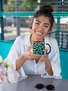 Mulher sorridente segurando uma caneca de porcelana com estampa animal print em um ambiente moderno.