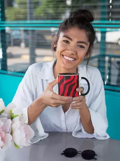 Mulher sorrindo enquanto segura uma caneca de porcelana com estampa animal print em cores vermelha e preta.