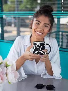 Mulher sorrindo enquanto segura uma caneca de porcelana com estampa animal print em preto e branco.