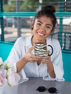 Mulher sorridente segurando uma caneca de porcelana com estampa de zebra em um ambiente moderno.