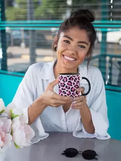 Mulher sorridente segurando uma caneca de porcelana com estampa animal print em rosa e preto.