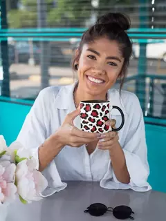 Uma mulher sorridente segurando uma caneca de porcelana com estampa animal print, em um ambiente moderno e iluminado.