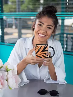 Mulher sorridente segurando uma caneca de porcelana com estampa animal print em um ambiente moderno.