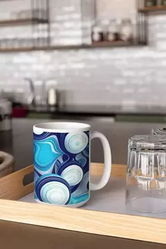 Caneca com design de bolas abstratas em azul e branco, posicionada em uma bandeja de madeira ao lado de um copo de vidro.