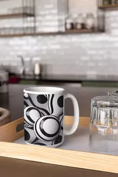 Caneca moderna com design de bolas abstratas em preto e branco, em uma bandeja ao lado de um copo.