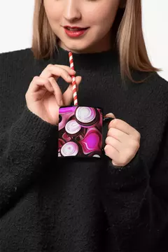 Mulher segurando uma caneca preta com design abstrato em tons de rosa e branco, usando um canudo listrado.